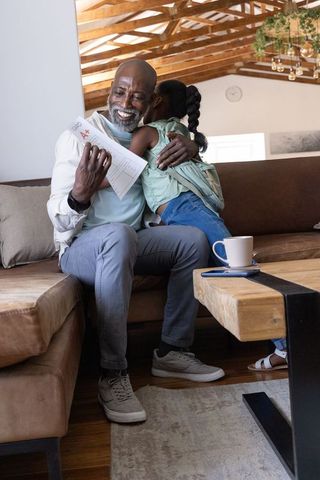 African american grandfather hugging granddaughter celebrating a+ report card, mask under chin
