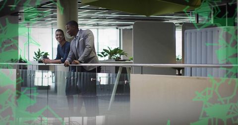 Two business colleagues leaning on glass balustrade in modern office sharing coffee