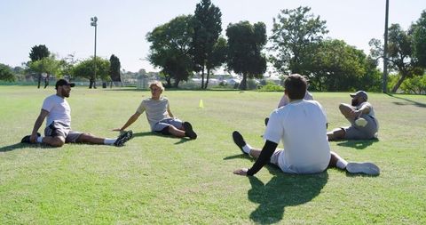 Multiracial men stretching in park circle during outdoor fitness training and team warmup