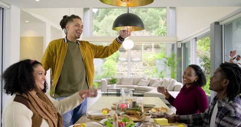 Multiracial friends toasting around modern dining table during bright home dinner gathering