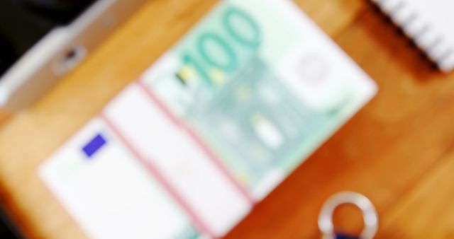 This image of blurry 100 Euro bills on a wooden desk conveys themes of finance, wealth, and monetary transactions. Could be used for financial blogs, economic insights, investment guides, European Union monetary discussions, or business proposals.