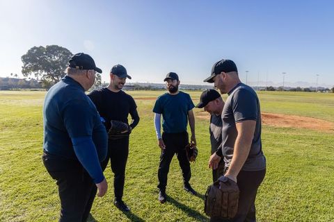 Adult baseball team huddling on sunny field before game, teammates holding gloves