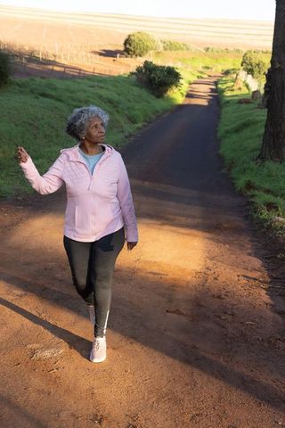Senior african american woman walking rural dirt lane in pink jacket during morning walk