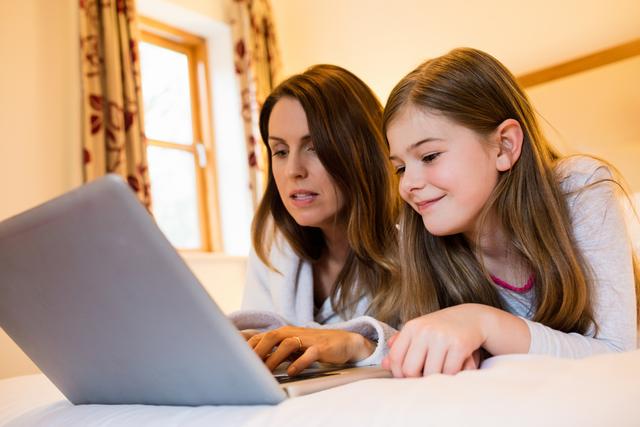 Mother and daughter using laptop in bedroom at home