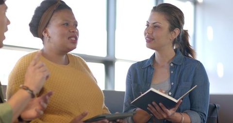 Multicultural women discussing project and taking notes in bright coworkorking space