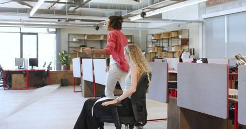 Colleagues Enjoying Playful Chair Ride in Open-Plan Office