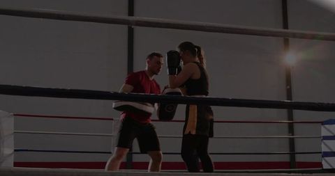 Female boxer training with coach holding focus mitts in boxing ring, intense pad work