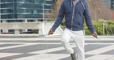 African American man jumping rope on urban plaza wearing navy hoodie and grey sweatpants