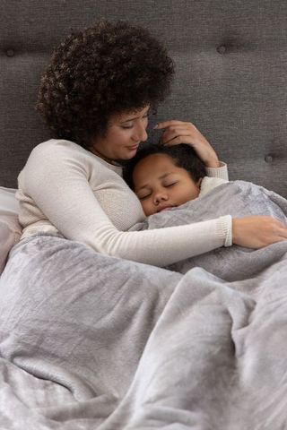 African american mother cradling sleeping child under plush gray blanket for cozy bonding