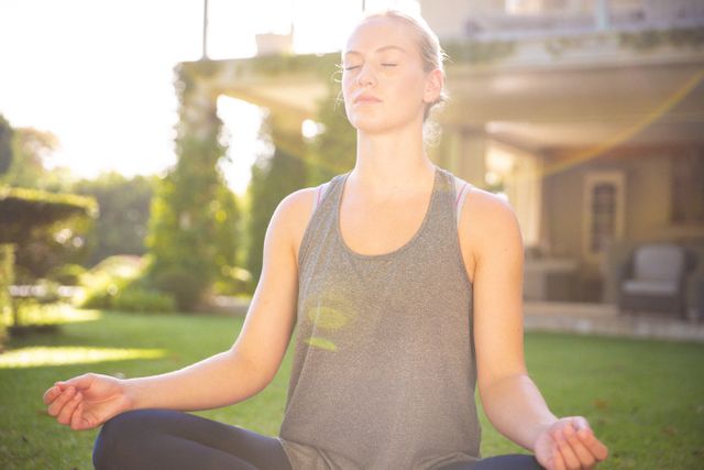 Caucasian woman practicing meditation in a garden during sunset. Ideal for content related to relaxation, mindfulness, wellness, outdoor activities, and healthy lifestyle. Can be used in articles, blogs, and advertisements promoting mental health, fitness, and peaceful living.