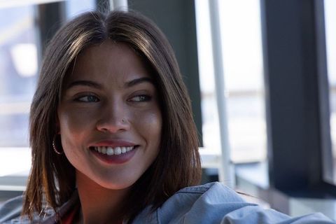 Smiling woman turning right wearing denim jacket and hoop earring in sunlit modern lounge