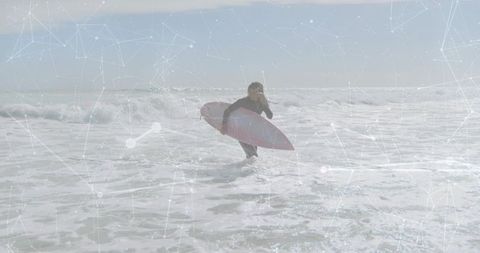 Surfer wading through breaking waves carrying pink longboard with digital network overlay