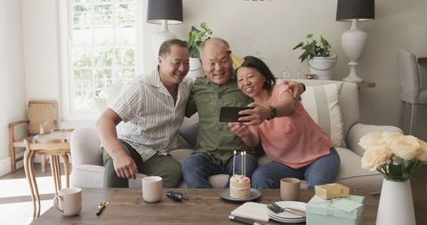 Cheerful Asian Seniors Celebrating Birthday with Cake and Selfie