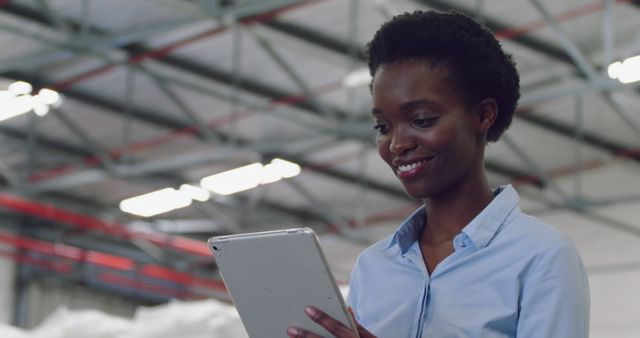 Young biracial woman reviews data on a tablet in a warehouse. She's focused on optimizing logistics and inventory management.