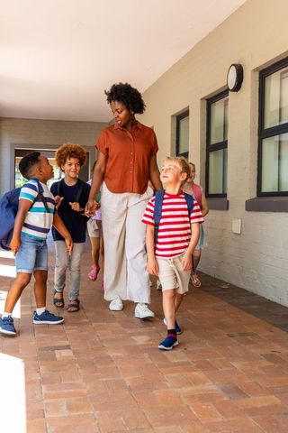 African american teacher leading diverse elementary kids walking sunlit school corridor