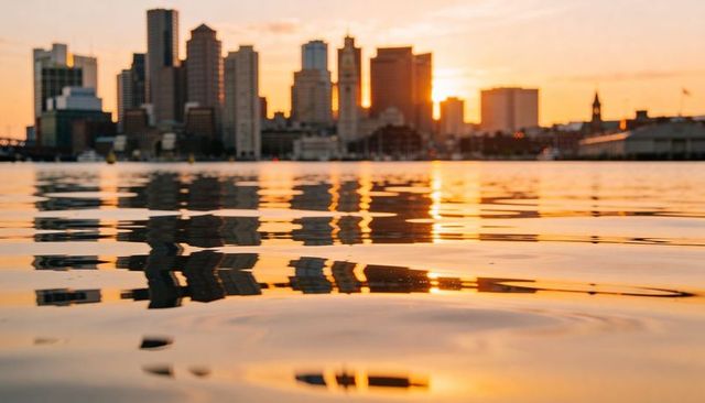 Golden sunset reflecting city skyline over rippling harbor water with silhouetted towers
