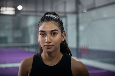 Focused indian female athlete on indoor purple court wearing black tank and gold hoops