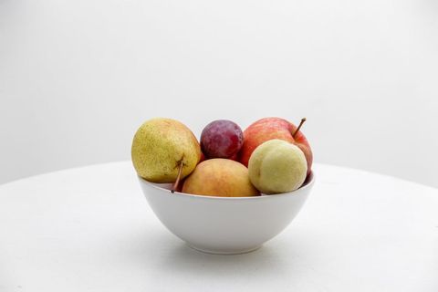 Displaying mixed fruit bowl with pears apples peaches and plum on clean white background
