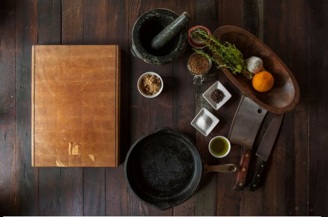 Rustic cooking preparation with various ingredients and utensils on wooden table presents an ideal setting for food blogs, recipe websites, culinary magazines, and cooking tutorials. Rich wooden surface and organized placement add warmth and invite viewers into a cozy cooking environment.