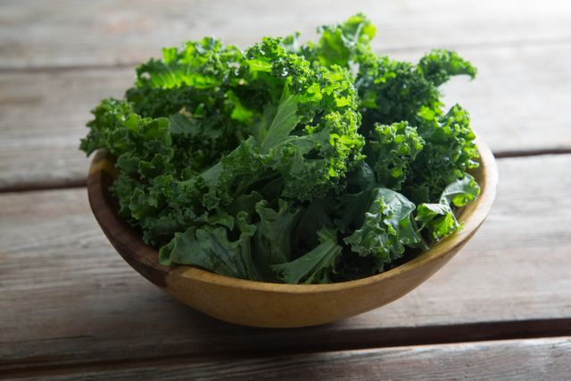 Fresh kale leaves in a wooden bowl on a rustic wooden table. Ideal for use in articles or advertisements about healthy eating, organic food, vegan and vegetarian diets, superfoods, and nutrition. Perfect for food blogs, recipe websites, and health magazines.
