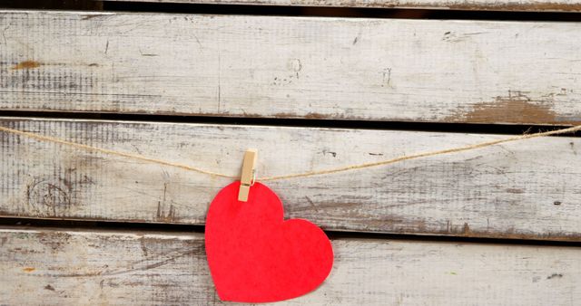 Picture showcases a red paper heart attached with a clothespin to a rope against a rustic wooden background. Ideal for Valentine’s Day cards, love-themed decorations, romantic social media posts, and DIY craft concepts.