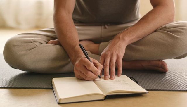 Man journaling cross-legged on yoga mat for mindfulness planning and daily reflection