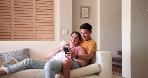Diverse male couple joyfully sharing engagement news at home