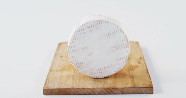 Round cheese wheel with soft, creamy texture sitting on wooden board with plain background. Ideal for use in food blogs, culinary websites, cheese advertising, restaurants' promotional materials, gourmet product marketing.