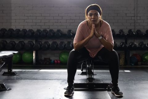 Focused African American Woman Sitting on Gym Bench Wearing Pink Top Preparing for Workout