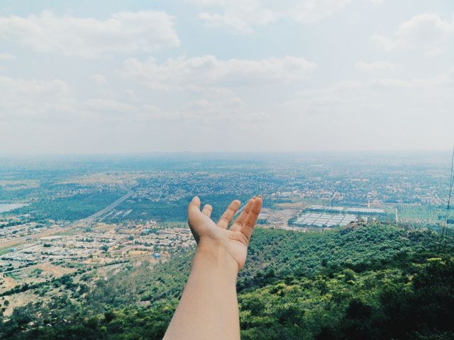 Person extending hand overlooking scenic city landscape. Perfect for travel blogs, urban exploration content, promotional material for tourism, or inspiration quotes. Ideal for emphasizing themes of freedom, adventure, and exploration.