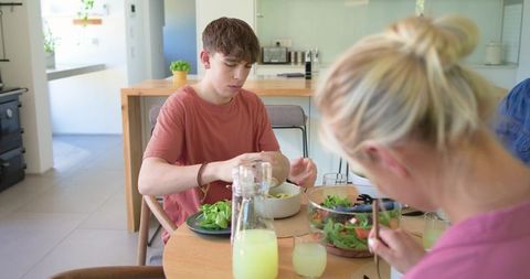 Teenager and woman sharing healthy lunch at sunlit round wooden kitchen table