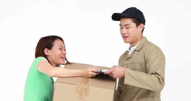 A young Asian delivery man is handing over a package to a young Asian woman, who is signing for it on a digital device, with copy space. Their interaction represents a common scene in logistics and e-commerce where customers receive their orders directly from couriers.