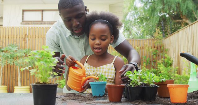 A father and his daughter are engaged in gardening outdoors. They are bonding while watering plants together in a backyard. This image is perfect for advertisements or articles about family bonding, outdoor activities, childcare, teaching children about nature, or home gardening tips.
