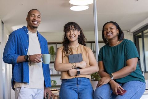 Smiling diverse coworkers collaborating at modern office island with tablet and coffee mug