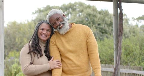 Smiling Black senior couple leaning together on garden patio wearing warm knit sweaters