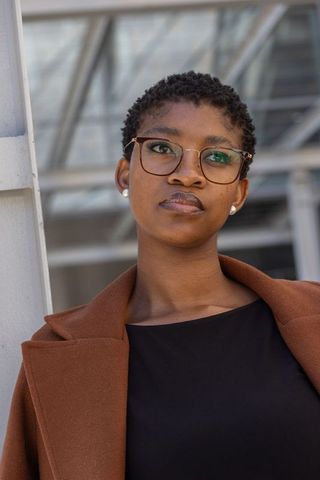 Confident african professional woman wearing glasses and brown coat looking up
