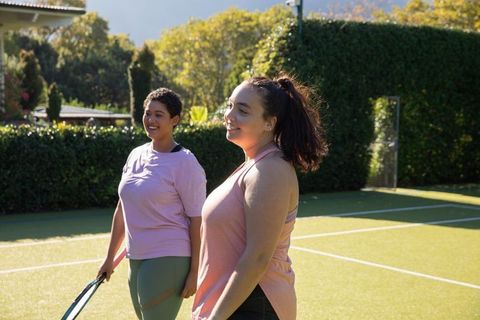Two friends chatting on sunlit tennis court in casual sportswear
