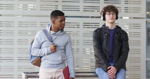 Young commuters waiting at transit shelter with backpack binder and headphones