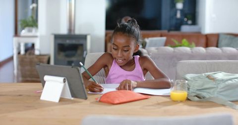 Elementary student doing homework with tablet and notebook at home study table