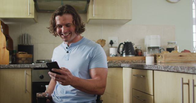 Young Man Smiling While Checking His Smartphone in Kitchen - Download Free Stock Images Pikwizard.com