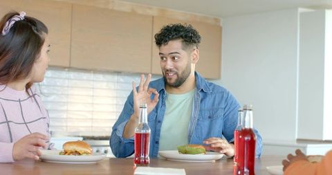Friends enjoying casual burger brunch at kitchen counter while man giving ok gesture