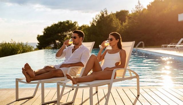Couple relaxing on loungers drinking cocktails by infinity pool at golden hour resort