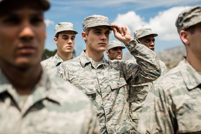 Group of military soldiers standing in formation at boot camp, wearing camouflage uniforms and hats. They appear focused and disciplined, ready for training or a mission. This image can be used for articles on military training, teamwork, discipline, and service. It is also suitable for recruitment campaigns, defense-related publications, and educational materials on military life.