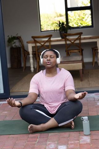 African american woman meditating with headphones on patio practicing mindfulness and yoga