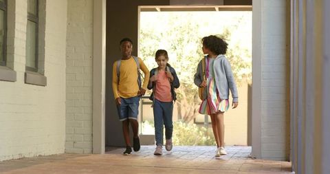Students walking through sunlit school breezeway carrying backpacks and chatting