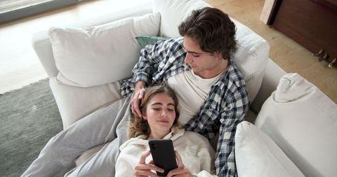 Relaxed couple lounging on sofa using smartphone at home