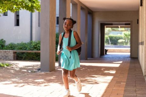 Young african american girl walking on campus walkway in turquoise dress carrying backpack