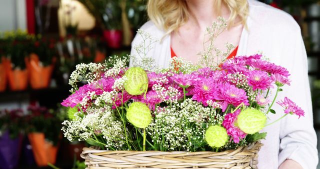 Woman holding a wicker basket filled with vibrant pink flowers and green foliage in a flower shop. Ideal for use in floral, gardening, and retail contexts. Can be used for marketing materials, advertisements, articles, or social media posts about florists, flower shops, flower arranging, and fresh flowers.