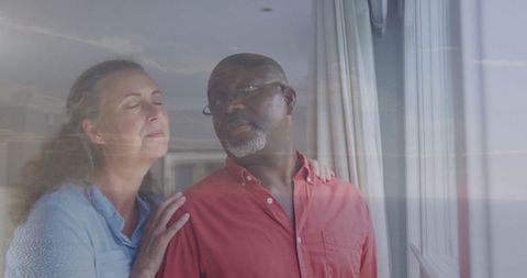 Senior couple gazing through glass window with reflective ocean view