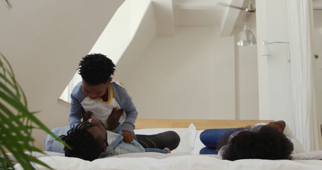 This image depicts an African American family spending quality time together at home, with a child playfully engaging with one parent while the other relaxes on the bed. Ideal for use in contexts such as family-oriented advertisements, articles on parenting, blog posts about home life, or marketing materials focusing on family and relationships.